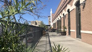 A pathway with a metal fence, a brick building with arched doorways, and a clear blue sky.