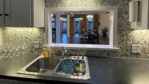 A kitchen with a large window, a sink with wine bottles, and a dining area visible through the window.