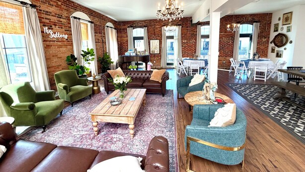 A spacious living room with a piano, green armchairs, a blue sofa, a wooden coffee table, and a chandelier.