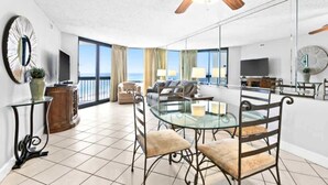 A spacious living area with a glass dining table, comfortable seating, a television, and a view of the ocean. - Beachfront 1BR condo in Destin with balcony, Gulf views and pool access (Destin)