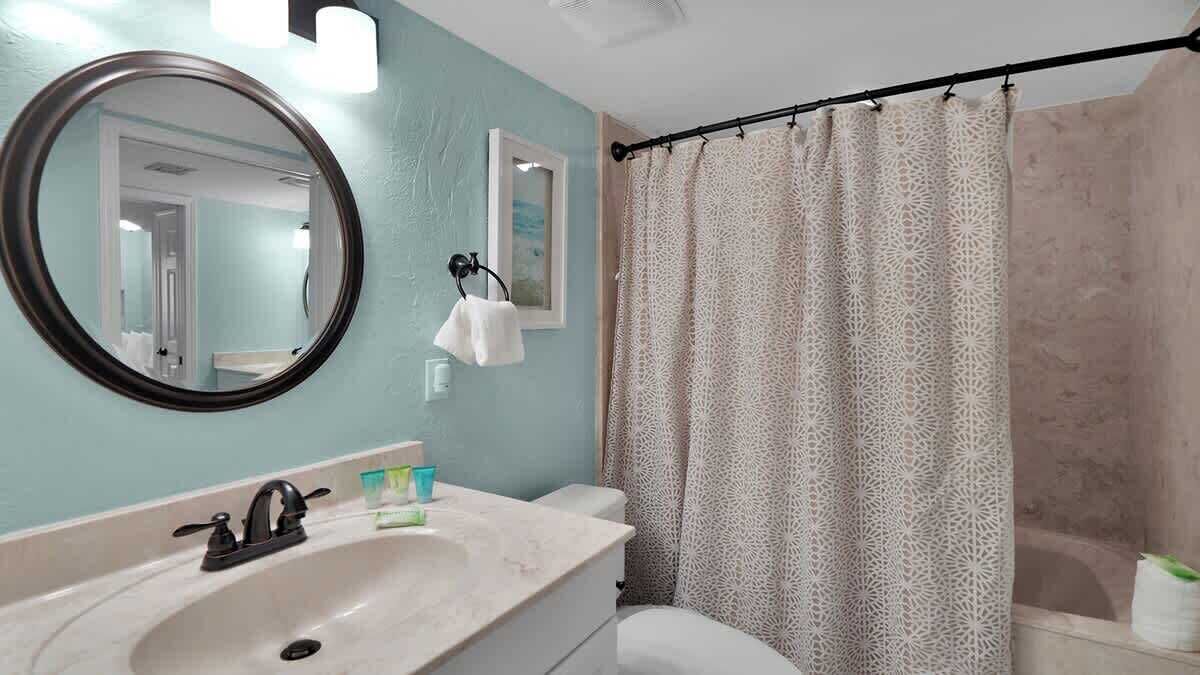 A bathroom with a round mirror, a sink, a toilet, and a shower curtain.