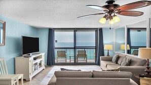 A hotel room with a balcony, a television, a sofa, and a ceiling fan.