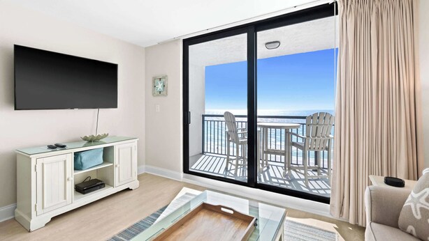 A room with a flat-screen TV, a white cabinet, a wooden tray, and a balcony with a view of the ocean. - 1BR Condo With Bright Interior and Gulf-View Balcony - SunDestin 0908 (Destin)