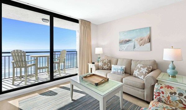Een balkon met uitzicht op de oceaan, een zithoek met een bank en stoelen, en een schilderij aan de muur.