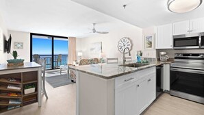 A modern kitchen with a large island, stainless steel appliances, and a view to the ocean. - 1BR Condo With Bright Interior and Gulf-View Balcony - SunDestin 0908 (Destin)