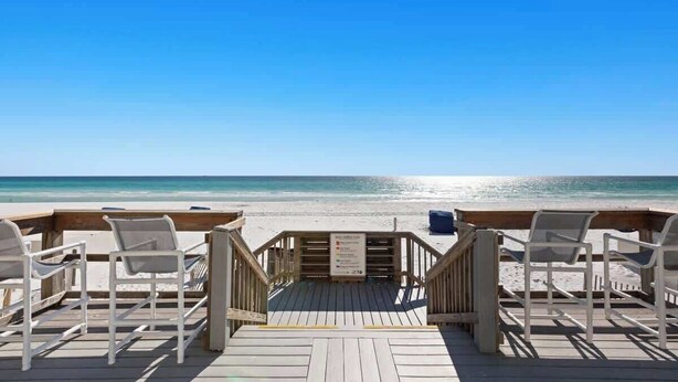 A wooden deck with white chairs facing a beach. - High-Floor 1BR Condo With Gulf Views, Balcony and Sleeps 4 (Destin)