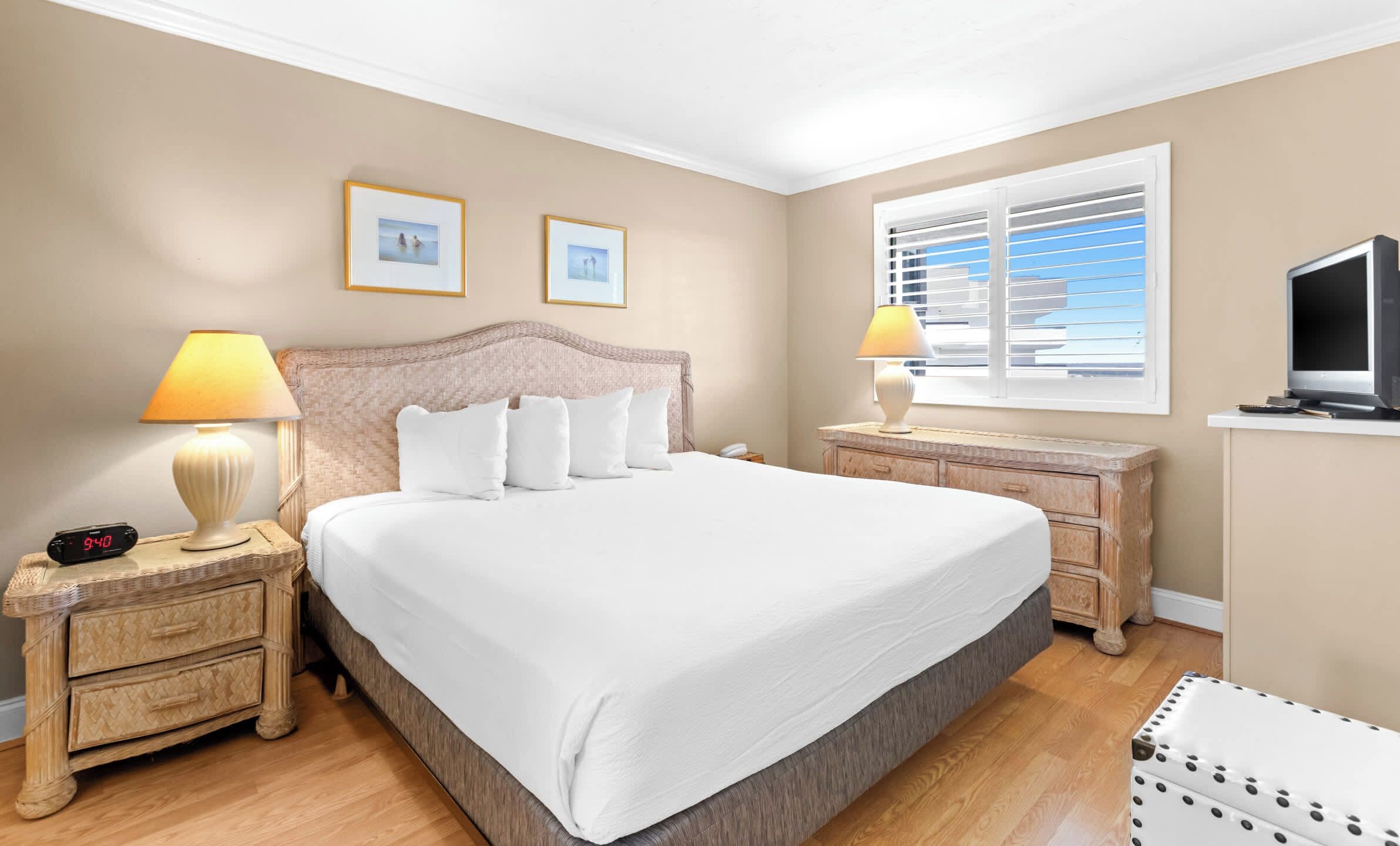 A hotel room with a large bed, two bedside tables, a TV, and a window with blinds.