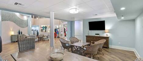 A spacious living area with a wooden dining table, wicker chairs, and a flat-screen TV mounted on the wall.
