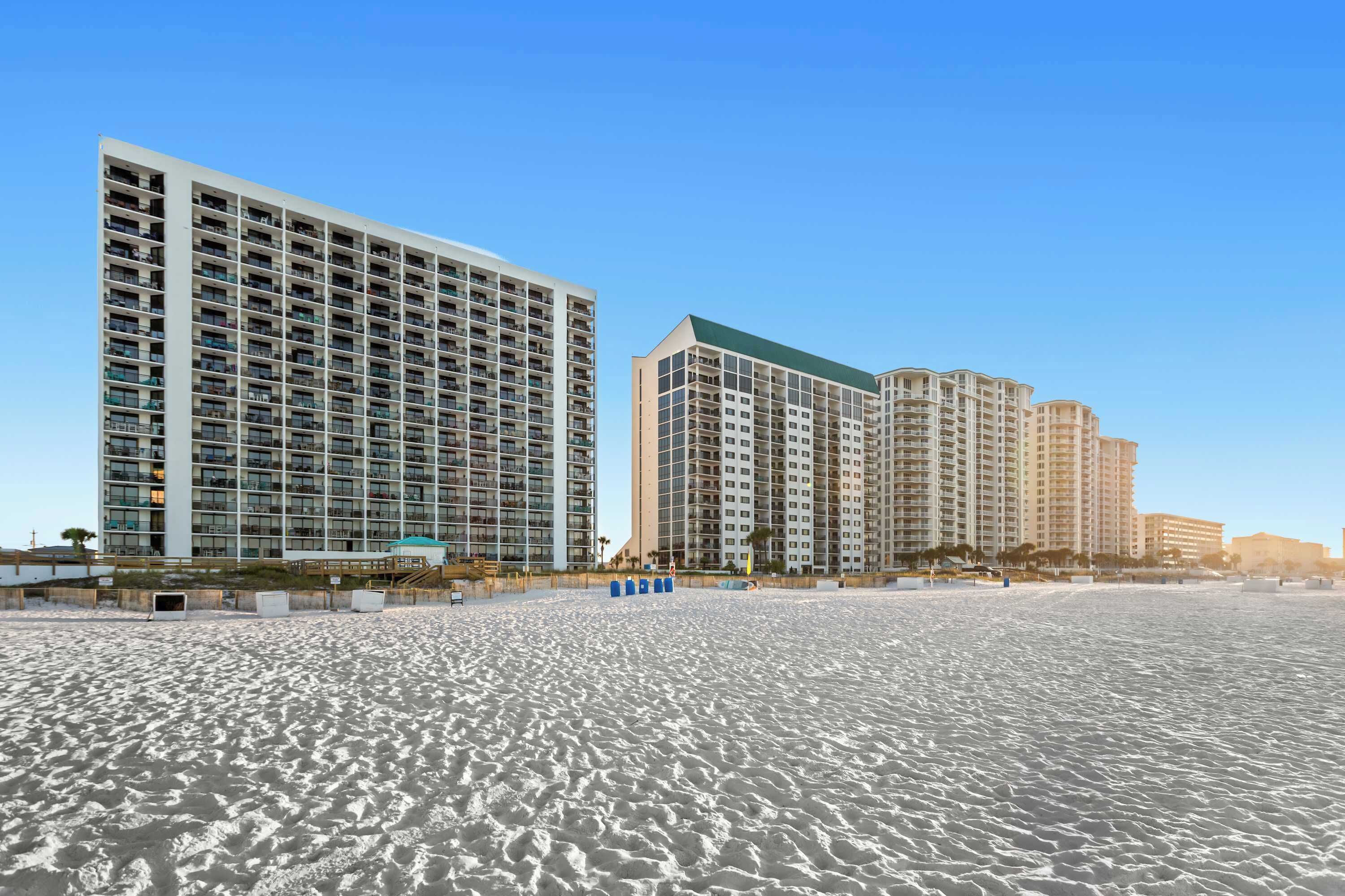 A beachfront hotel with multiple high-rise buildings, sandy beach, and clear blue sky.