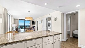 A modern kitchen with granite countertops, a built-in washing machine, and a dining area with a view. - SunDestin 2BR Condo With Panoramic Gulf Views and Sleeps 7 - Unit 0601 (Destin)