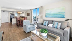 A modern living room with a grey sofa, a glass coffee table, and a dining area with wooden chairs. - SunDestin 2BR Condo With Panoramic Gulf Views and Sleeps 7 - Unit 0601 (Destin)
