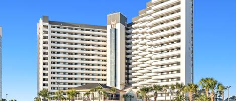 A multi-story hotel with a parking lot in front, featuring a modern design with balconies.
