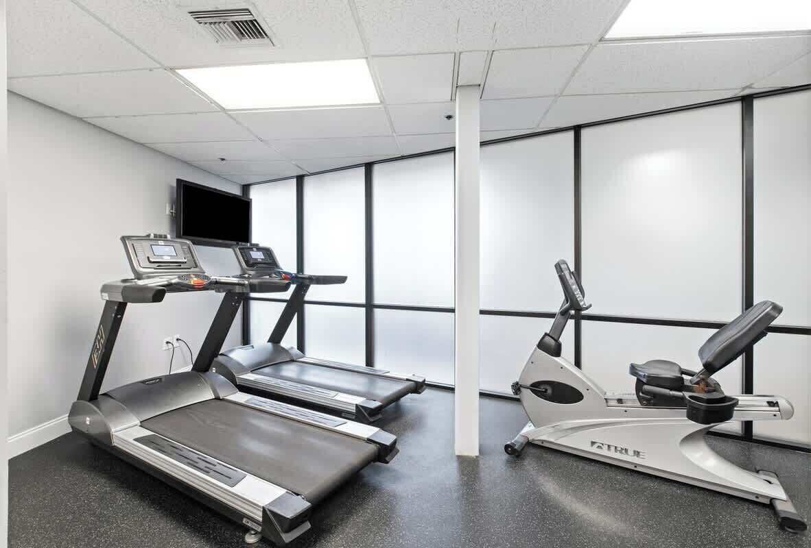 Une salle de remise en forme équipée de tapis de course et d’un appareil elliptique, dotée de grandes fenêtres et d’un téléviseur à écran plat.