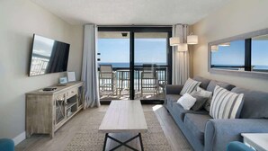 A modern living room with a sofa, a coffee table, a TV, and a balcony with a view of the sea. - SunDestin Resort Unit 0712 (Destin)