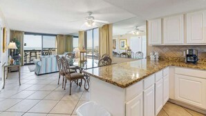 A spacious kitchen with a granite countertop, white cabinets, and a dining area with a glass table and chairs. - SunDestin 1BR Condo With Gulf-Front Sunrise and Sunset Views - Unit 0618 (Destin)
