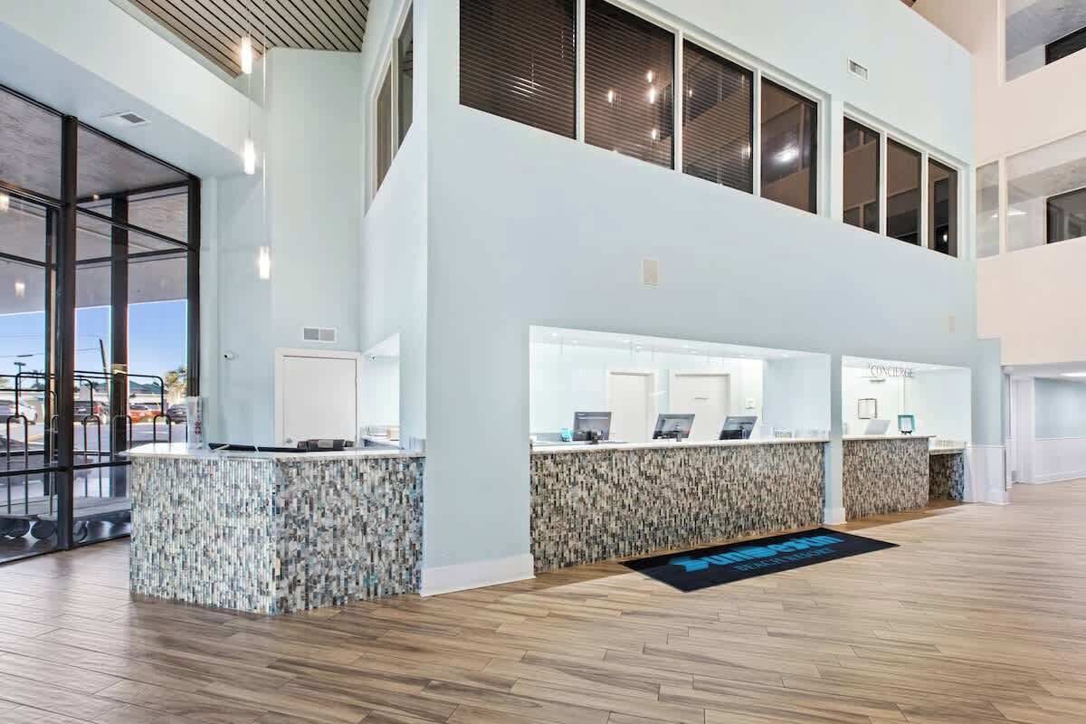 Una moderna area reception di un hotel con un design a due piani, caratterizzata da un banco reception centrale, diverse postazioni computer e un'ampia entrata in vetro.