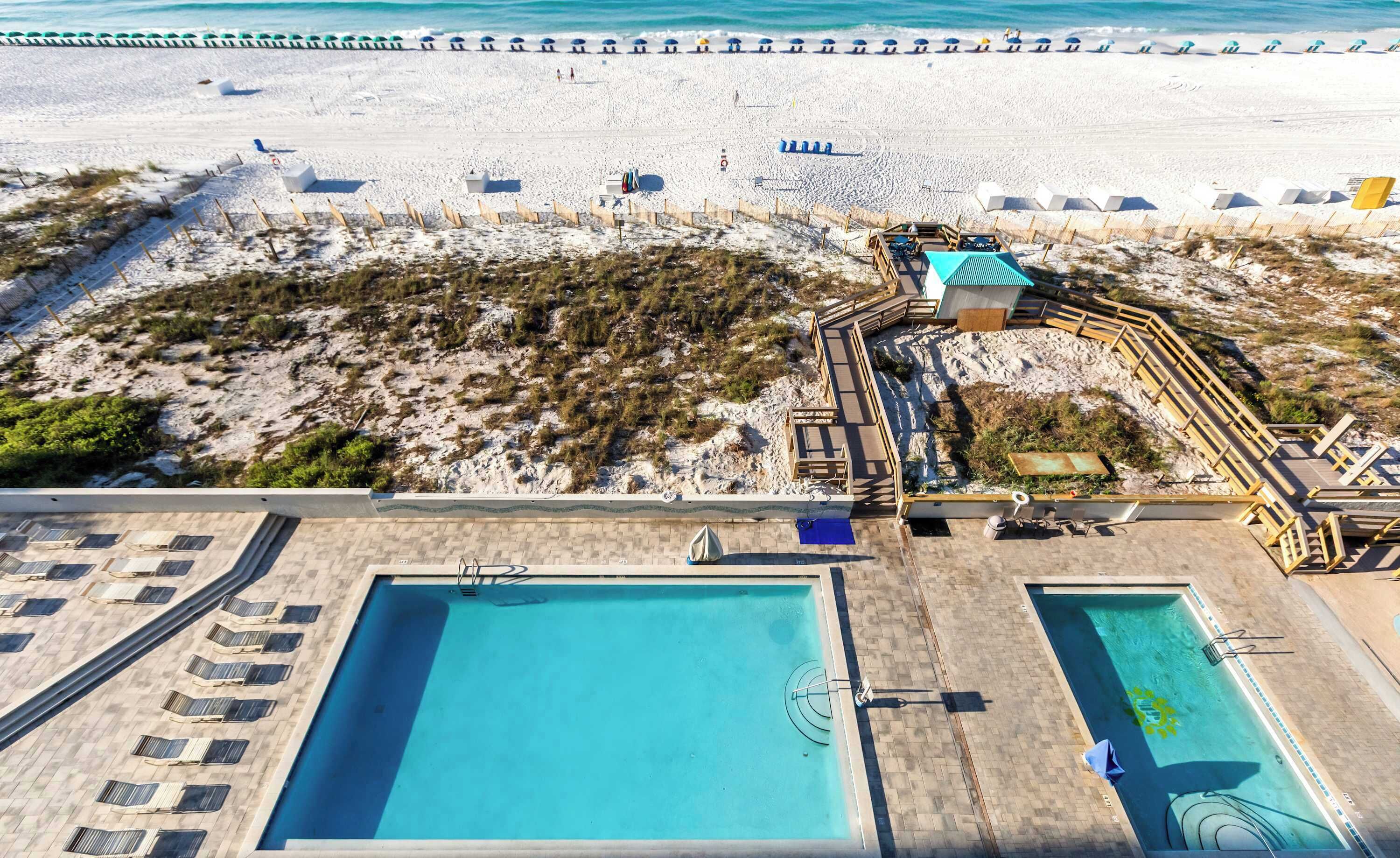 An aerial view of a beach resort with a swimming pool, sun loungers, and a lifeguard tower.