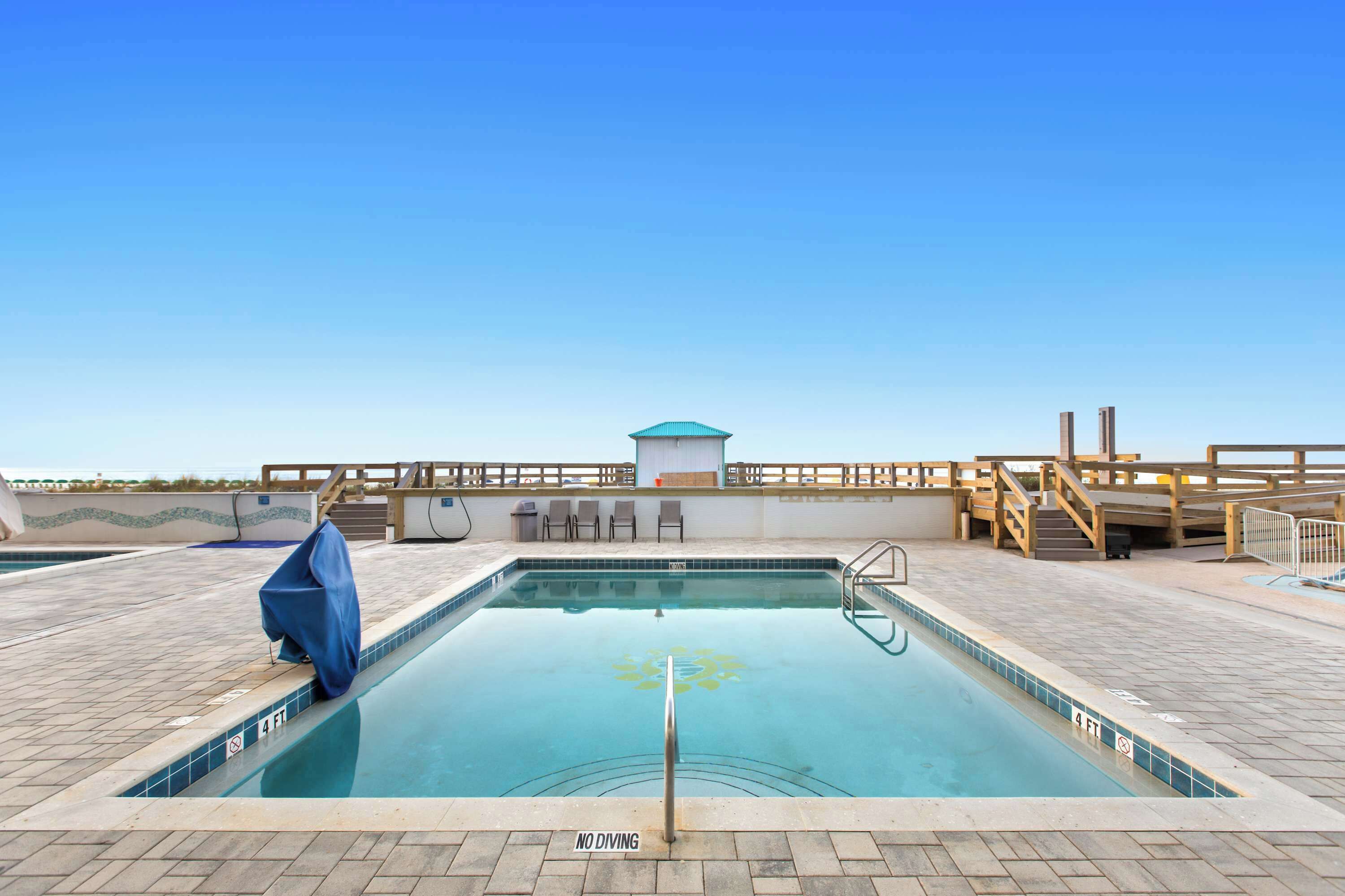 A swimming pool with a 'NO DIVING' sign, a covered bench, and a wooden deck with a view of the ocean.