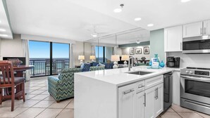 A modern kitchen with a central island, a dining area with a view, and a living room with a sofa and lamps.