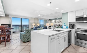 A modern kitchen with a central island, a dining area with a view, and a living room with a sofa and lamps.
