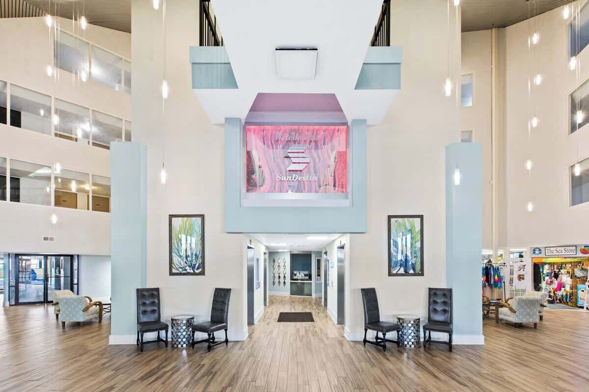 A spacious lobby with a central reception desk, multiple seating areas, and a view of the Sea Store in the background.