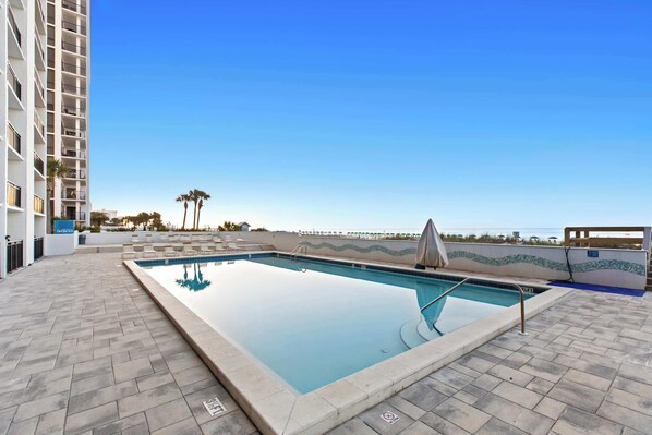 Une piscine sur le toit, avec une eau d’un bleu limpide, entourée d’une terrasse carrelée, et un immeuble de grande hauteur en arrière-plan.
