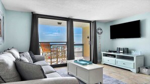 A living room with a sofa, a coffee table, a TV, and a balcony with a view. - SunDestin 1BR Retreat With Bunk Beds and Gulf-View Balcony - Unit 0305 (Destin)