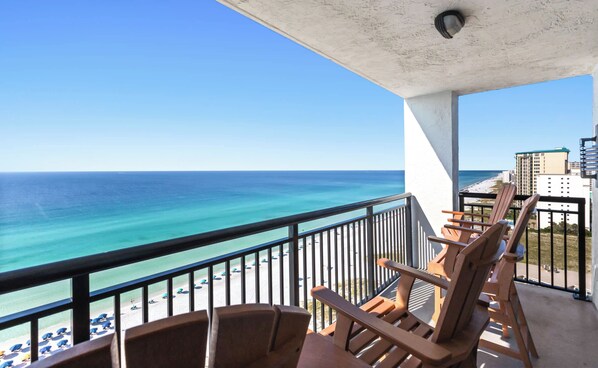 Ein Balkon mit Blick auf das Meer und den Strand, Holzstühle und ein Geländer.