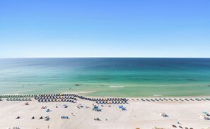 A beach with rows of umbrellas and sun loungers, a clear sky, and calm sea. - SunDestin High-Floor 2BR Condo With Gulf Views and Private Balcony (Destin)