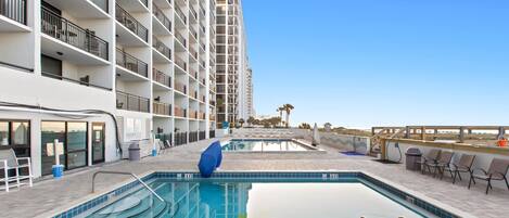 A swimming pool with a view of a high-rise building, outdoor seating, and a clear sky.
