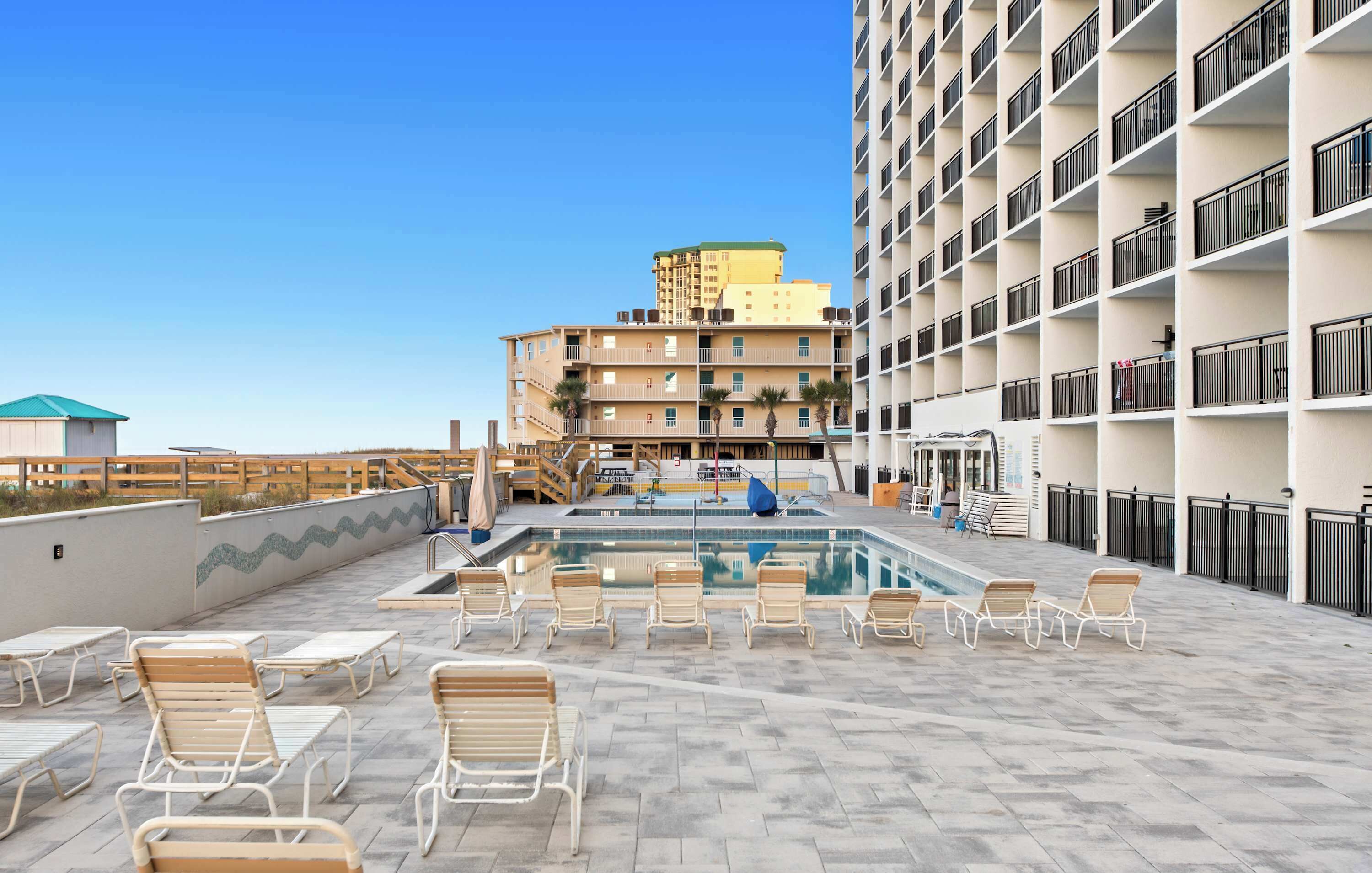 Un área de piscina en la azotea con sillones de descanso, piscina y un edificio con balcones al fondo.