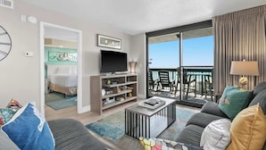 Ein modernes Wohnzimmer mit Flachbildfernseher, einer Couch, einem Couchtisch und einem Balkon mit Gartenmöbeln.