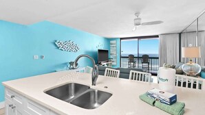 A modern kitchen with a large sink, white cabinets, and a view of the ocean through large windows.