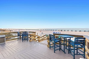 A wooden deck with tables and chairs overlooking a beach.