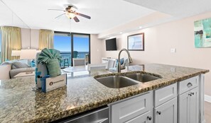 A modern kitchen with a granite countertop, stainless steel sink, and a ceiling fan.