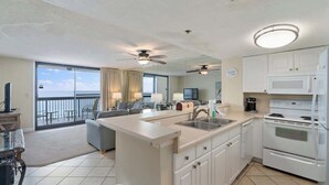 A modern kitchen with a central island, a dining area with a view, and a balcony with a pool. - SunDestin Beach Retreat With Bright Open Living and Gulf Scenery (Destin)