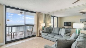 A hotel room with a balcony, a gray sofa, a TV, and a desk with a lamp. - SunDestin Beach Retreat With Bright Open Living and Gulf Scenery (Destin)