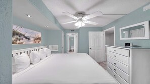 Une chambre à coucher avec un grand lit, un ventilateur de plafond, une commode et un tableau accroché au mur.