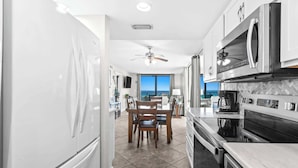 A modern kitchen with a dining area, large windows, and a view of the ocean.