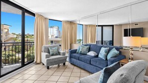 A modern living room with a sofa, armchair, and a view of the cityscape through large windows. - SunDestin Beach Retreat With Spacious Balcony Seating for 4 - Unit 0317 (Destin)