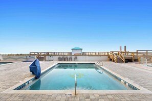 A swimming pool with a 'NO DIVING' sign, a covered bench, and a wooden deck with a view of the ocean.