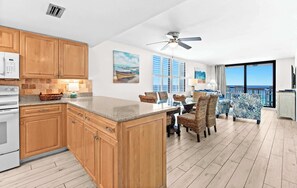 A modern kitchen with wooden cabinets, a granite countertop, and a dining area with wicker chairs.
