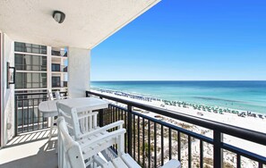 A balcony with white furniture, a view of the beach, and a clear blue sky.