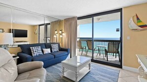 A hotel room with a balcony, a sofa, a coffee table, and a TV. - SunDestin Resort Unit 1407 (Destin)