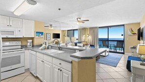 A modern kitchen with white cabinets, a granite countertop, and a view of the ocean through large windows. - SunDestin Resort Unit 1407 (Destin)