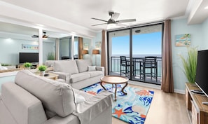 A modern living room with a sofa, a coffee table, and a balcony with a view of the sea.