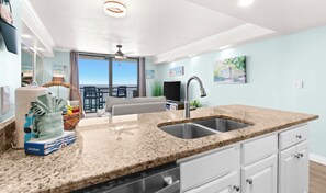 A modern kitchen with granite countertops, a dishwasher, and a sink. There is a dining area with a table and chairs, and a balcony with a view of the ocean. - SunDestin Resort Unit 1505 (Destin)