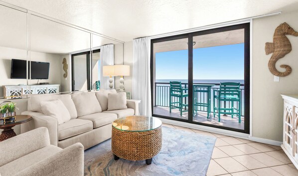 A living room with a sofa, a coffee table, and a view of the ocean through large sliding doors.
