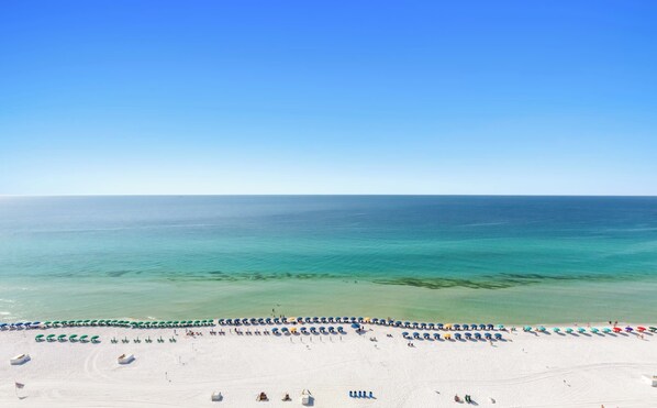 A beach with rows of umbrellas and a clear view of the ocean. - Relax Above the Coast at SunDestin 1805 (Destin)