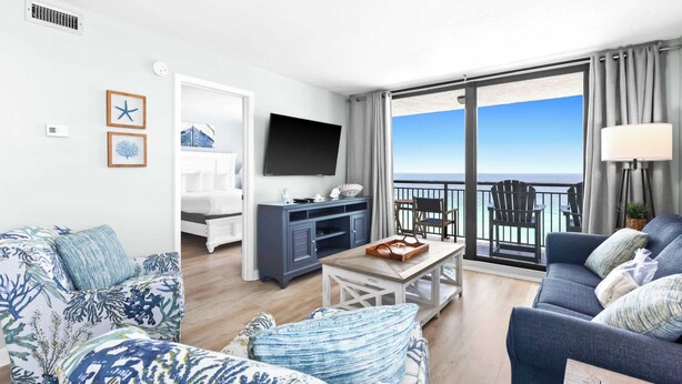 A modern living room with a balcony overlooking the sea, a flat-screen TV, and a cozy seating area. - SunDestin Resort Unit 1112 (Destin)
